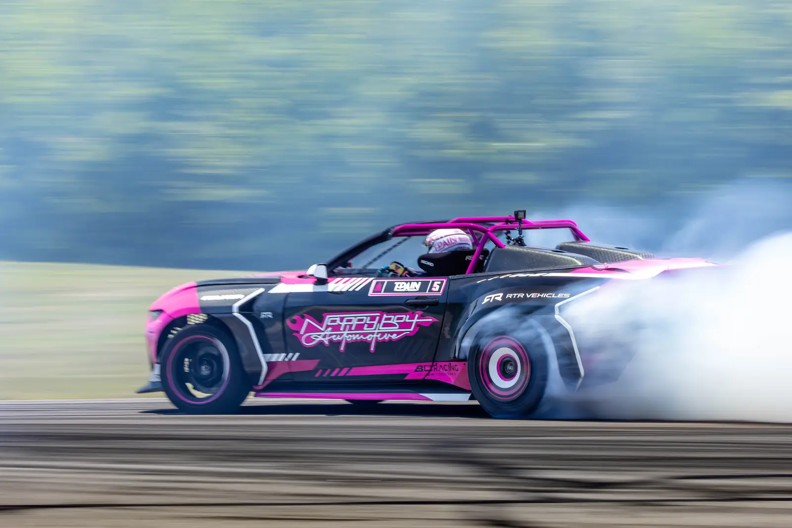 A pink and black drift car at full lock in a cloud of tire smoke